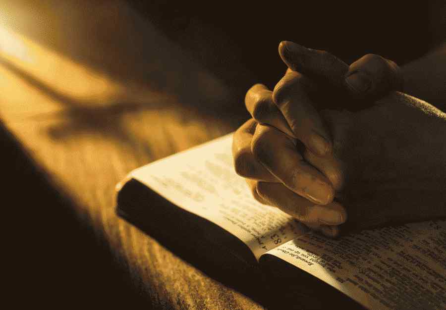 Nahaufnahme von gefalteten Händen auf offener Bibel